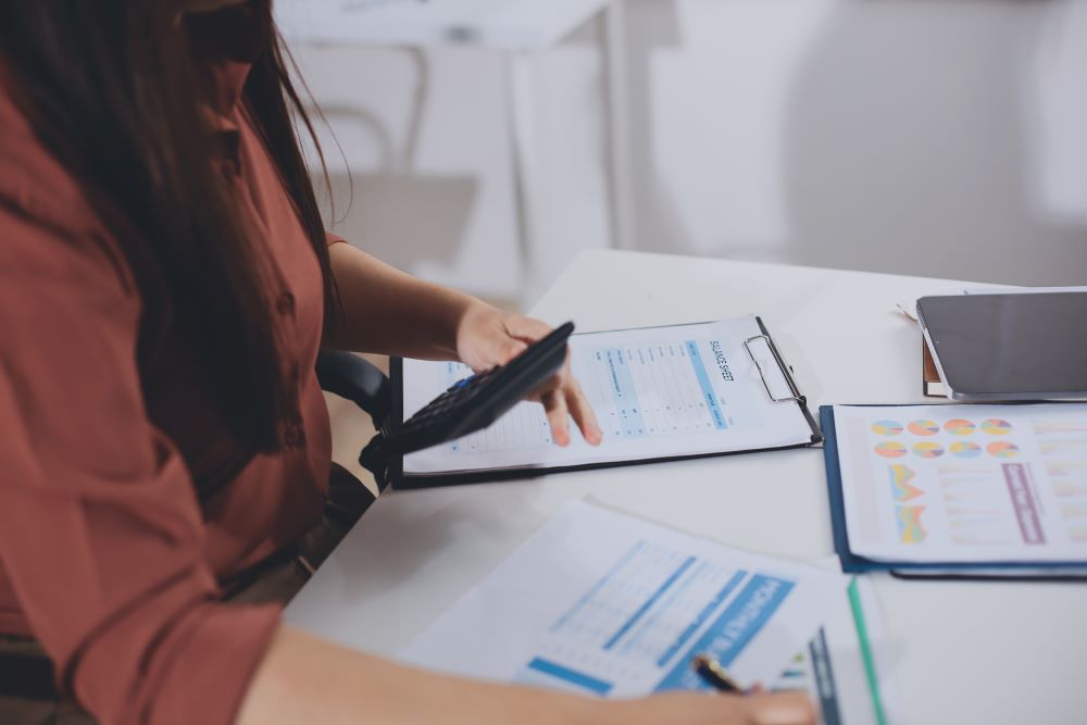 Profissional utiliza calculadora e analisa planilhas financeiras em mesa de escritório, representando bpo folha de pagamento.