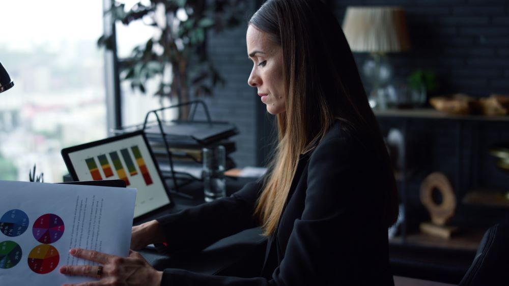 Gestora de RH analisando relatórios e gráficos da folha de pagamento em escritório corporativo, avaliando riscos trabalhistas e conformidade legal da empresa.