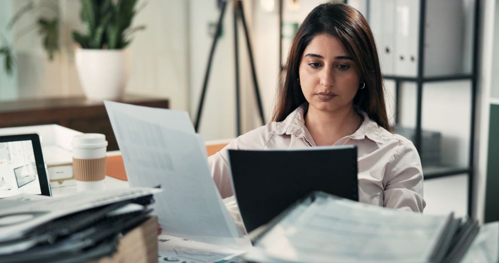 Profissional de RH analisando documentos e relatórios em mesa de escritório, representando a revisão de erros na folha de pagamento e o controle de processos no departamento pessoal.